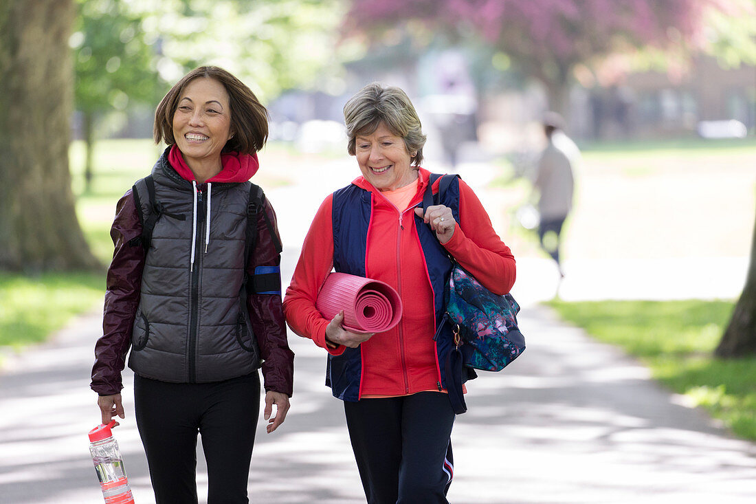 Active senior women friends with yoga mat walking