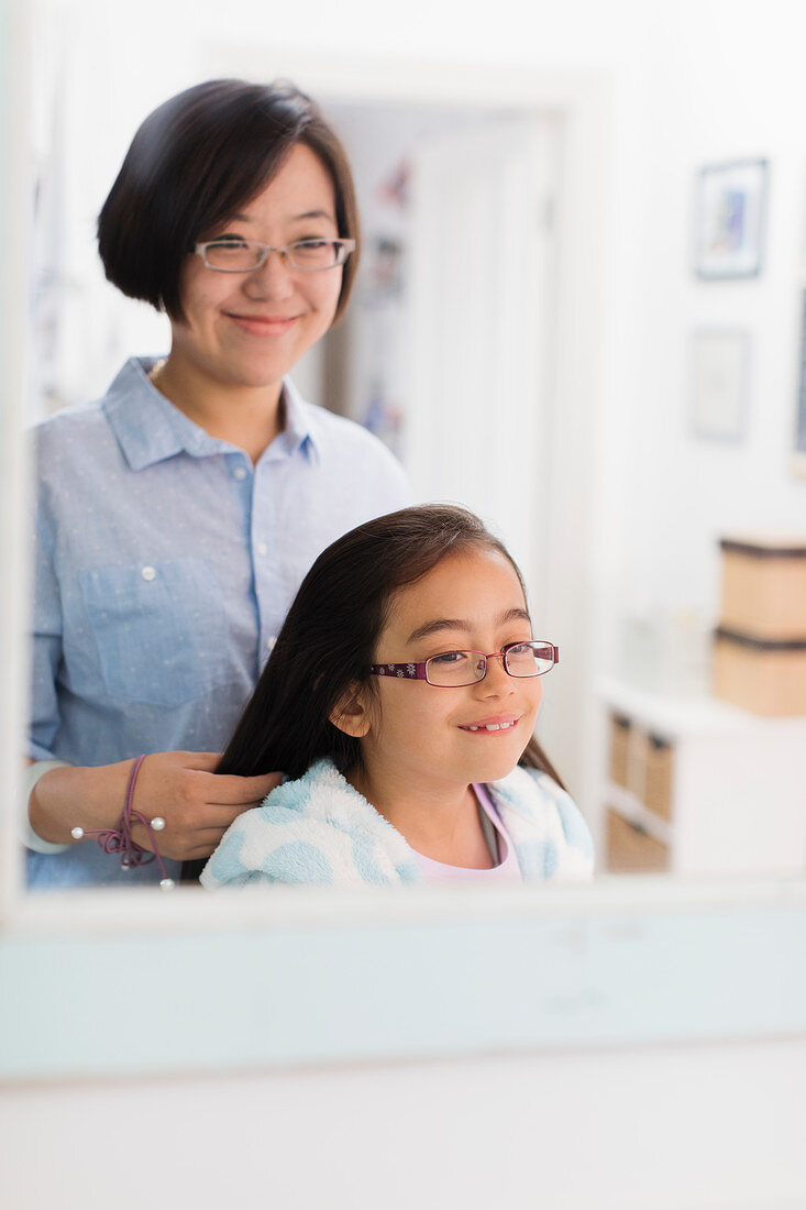 Mother fixing daughters hair in bathroom mirror