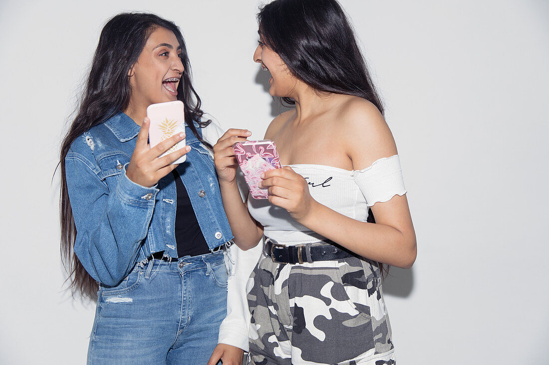 Laughing teenage twin sisters using smart phones