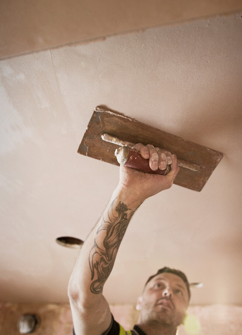 Construction worker with tattoo plastering ceiling