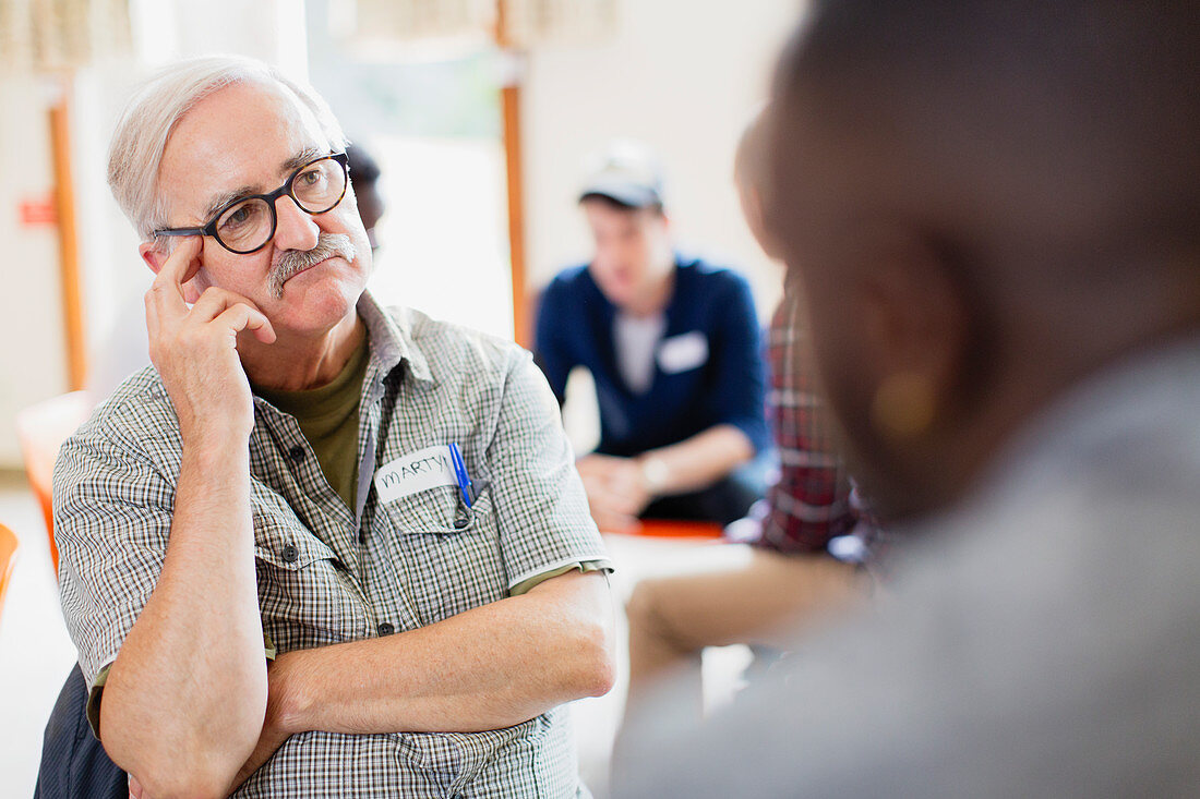 Attentive senior man listening in group therapy