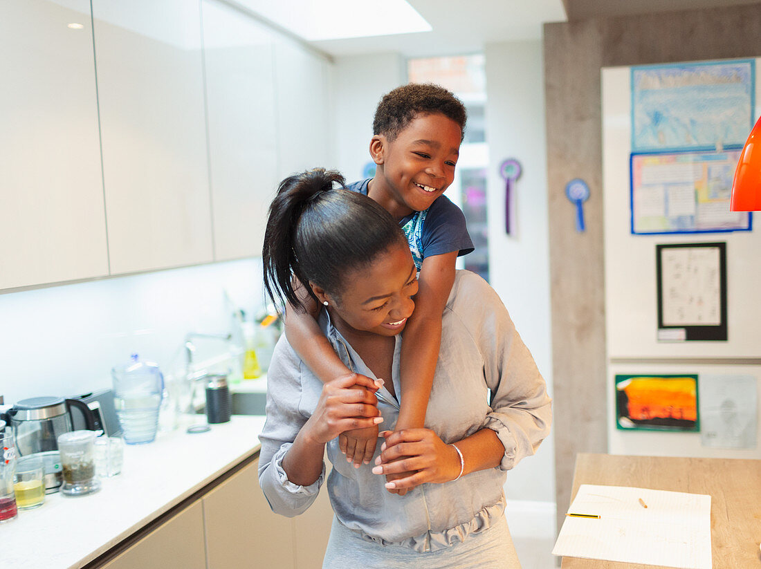 Playful mother and son piggybacking in kitchen