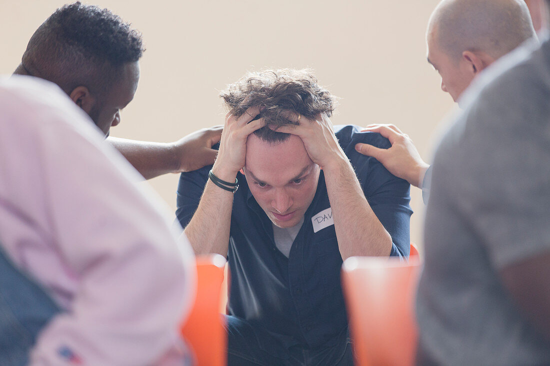 Men comforting upset man in group therapy