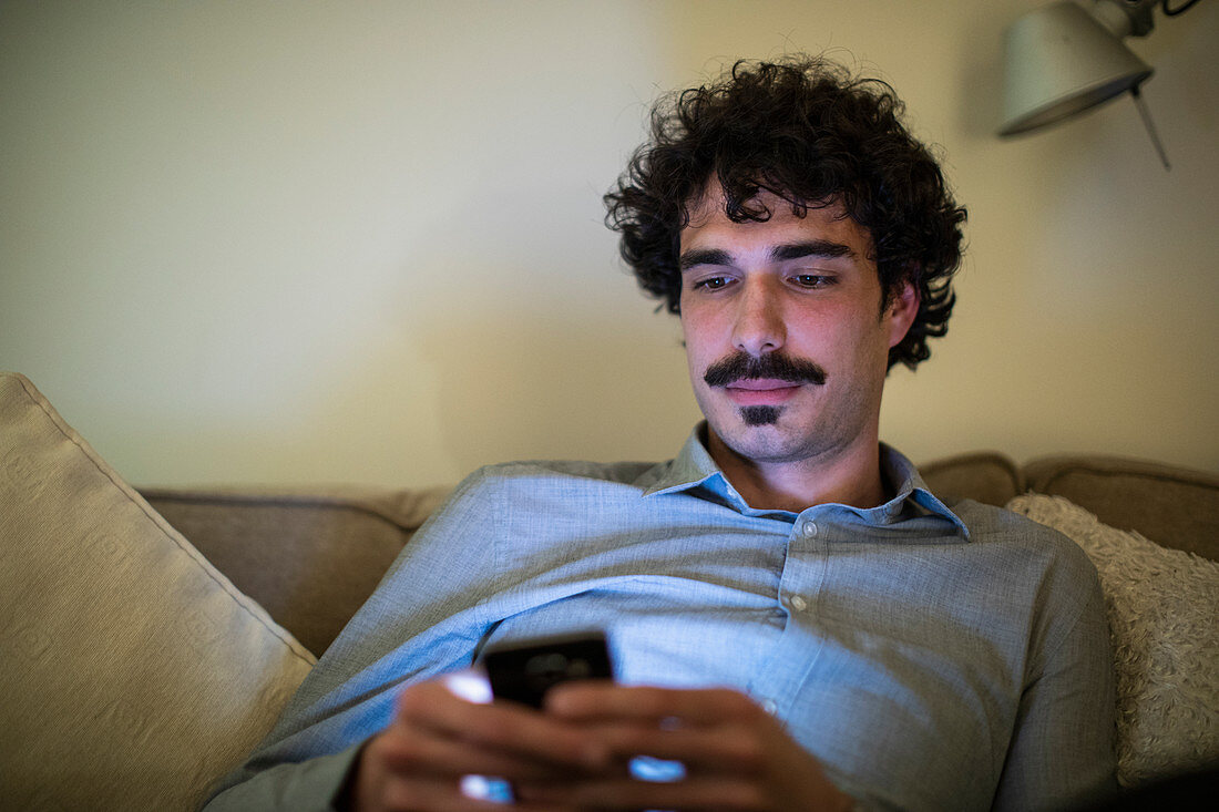 Man using smart phone on sofa at night