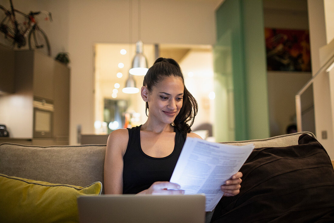 Woman reading paperwork at laptop