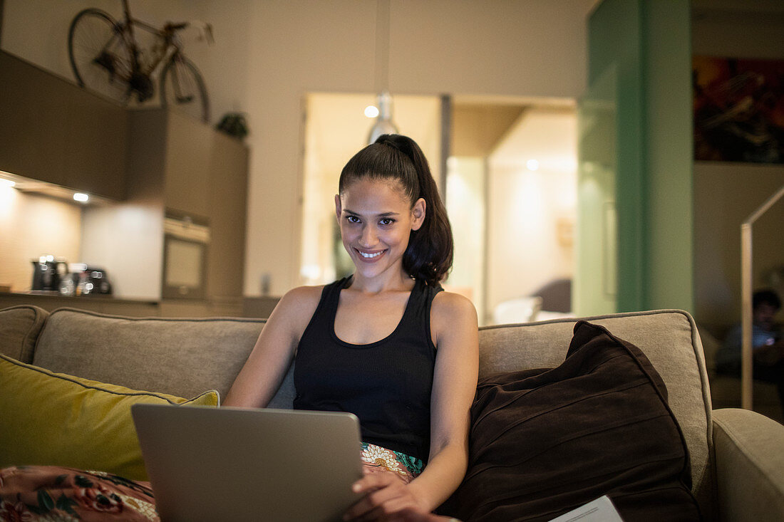 Portrait smiling woman using laptop on apartment sofa