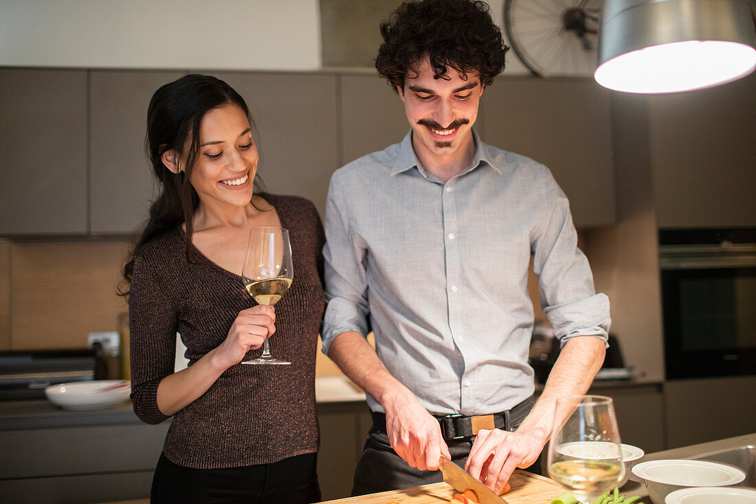 Happy couple preparing dinner and drinking white wine