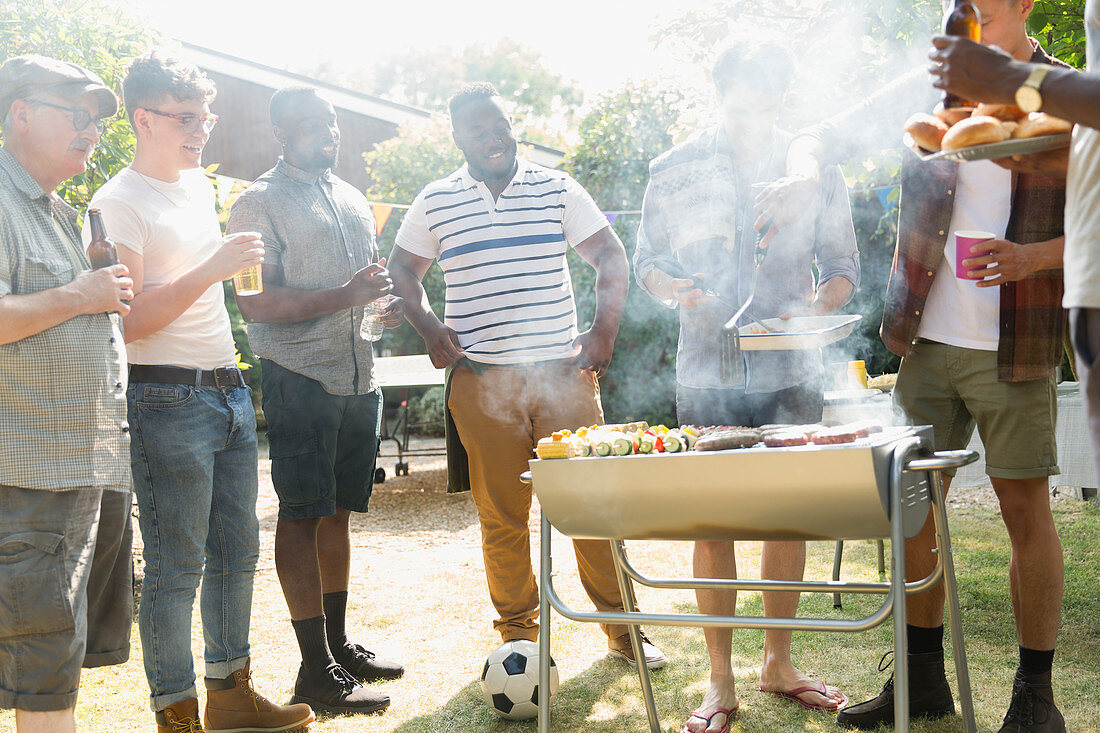 Male friends drinking beer and barbecuing in backyard