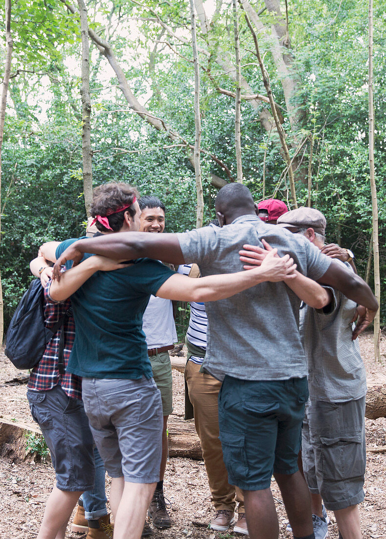 Men's group hugging in huddle, hiking in woods
