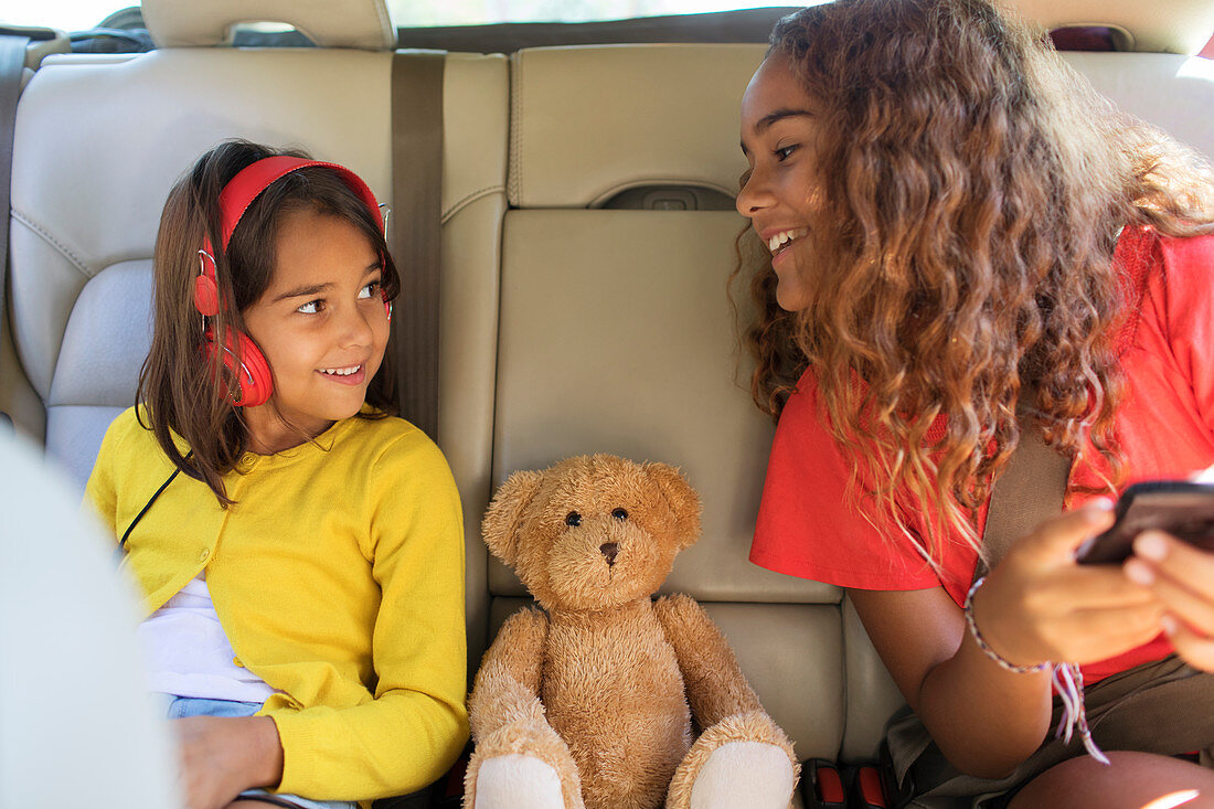 Sisters and teddy bear riding in back set of car