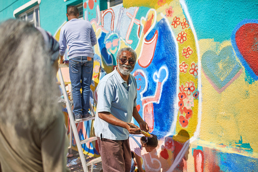 Senior man volunteer painting vibrant mural on wall