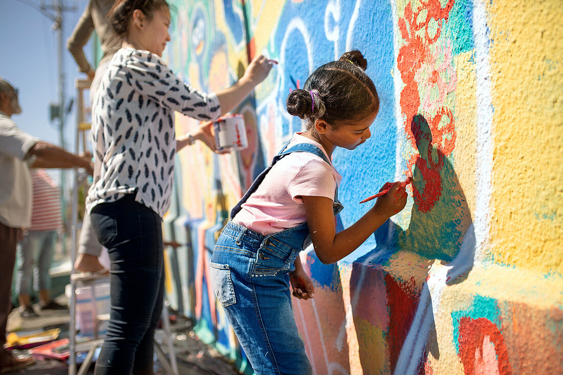 Girl volunteer painting vibrant mural on wall