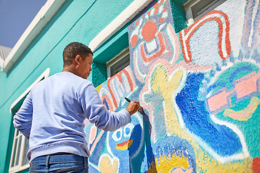 Male volunteer painting vibrant mural on wall