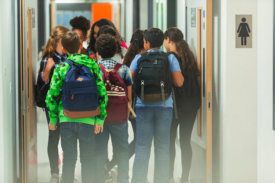 students with backpacks walking in school corridor