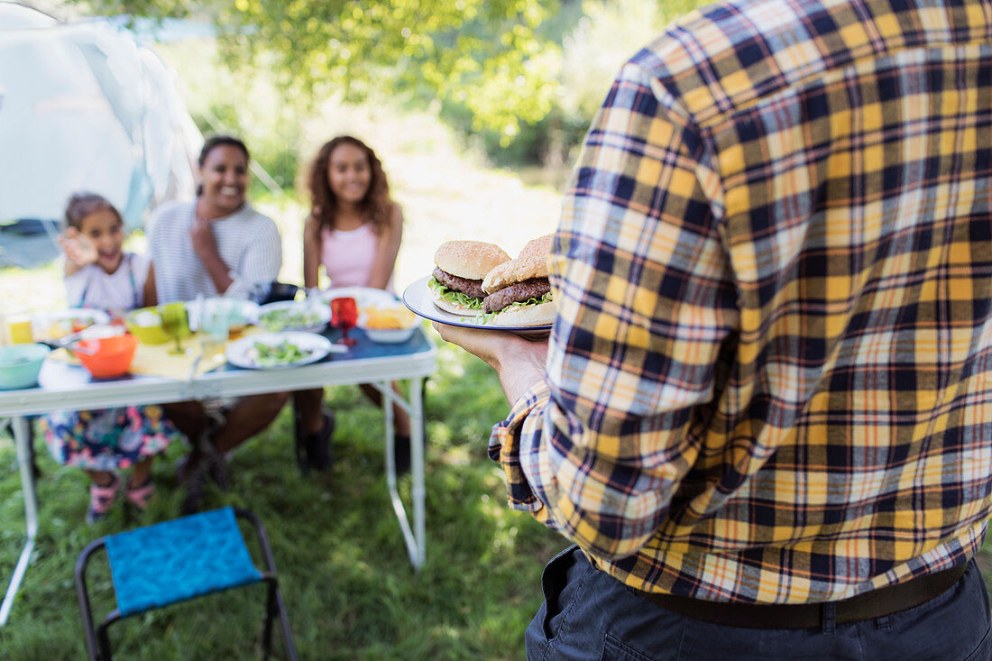 Father serving barbecue hamburgers to family table