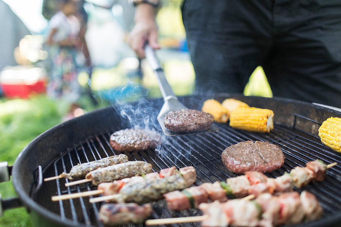 Man barbecuing hamburgers, kebabs and corn cobs