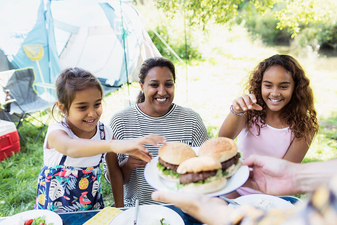 Happy mother and daughters reaching for barbecue hamburgers