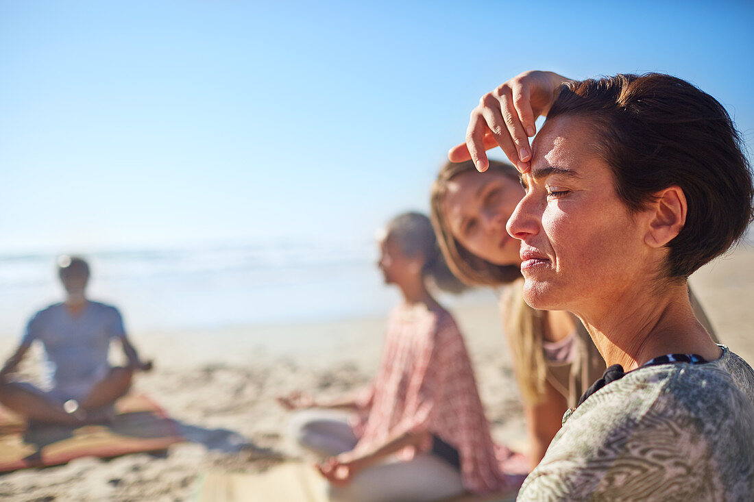Yoga instructor touching third eye of woman meditating