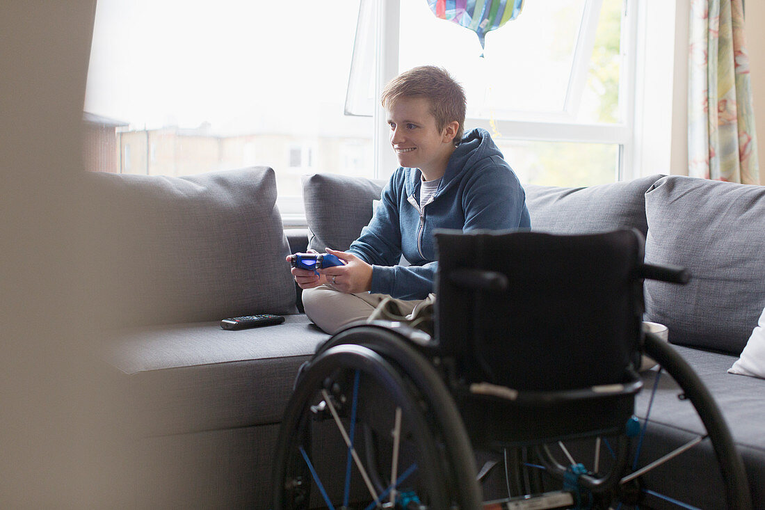 Young woman playing video game on sofa next to wheelchair