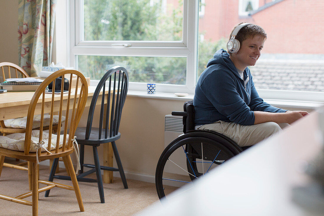 Young woman in wheelchair listening to music at window