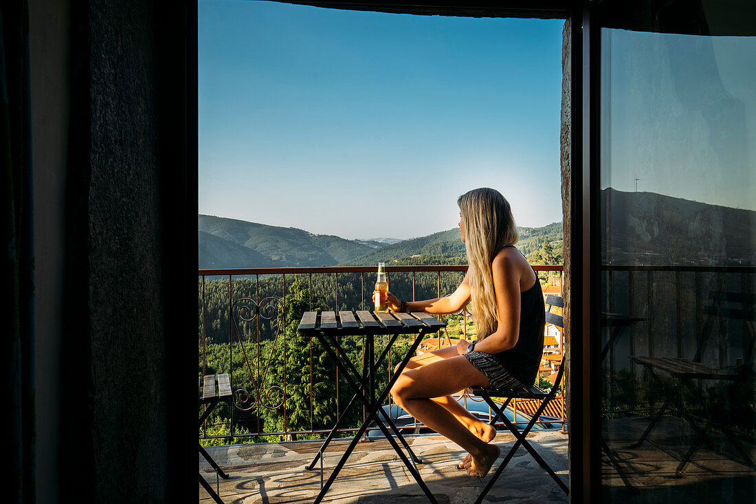 Woman relaxing, drinking beer on balcony