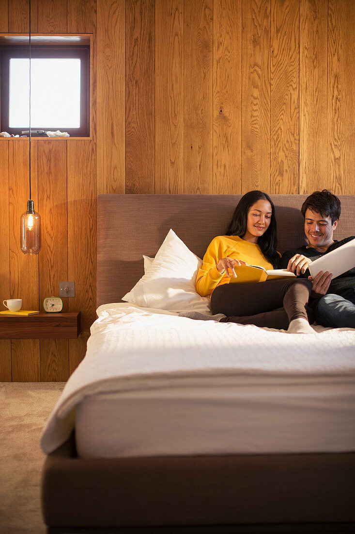 Couple reading book and using digital tablet in bed