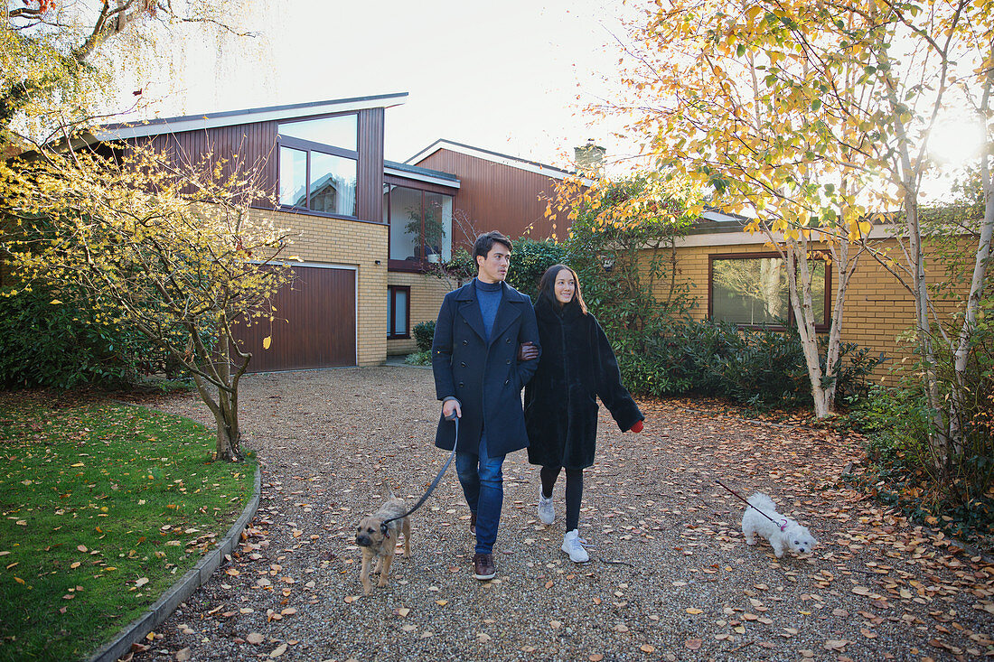 Couple walking dogs in autumn driveway