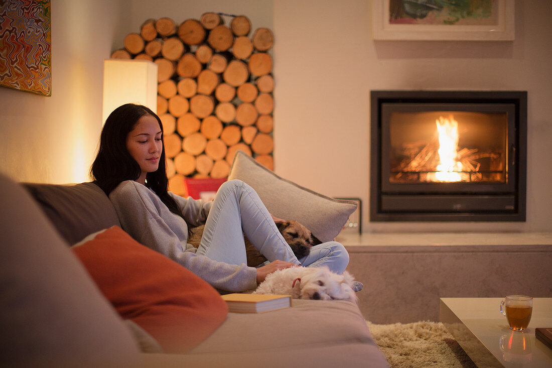 Young woman relaxing on sofa with dogs by fireplace
