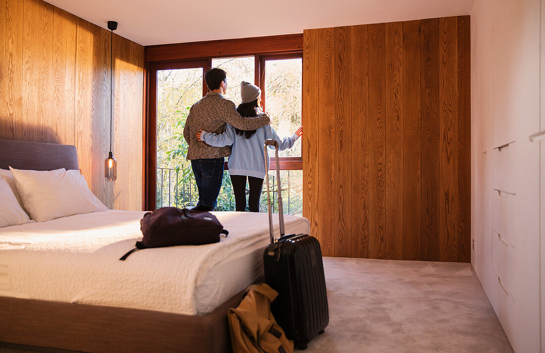 Couple with suitcase looking out bedroom window