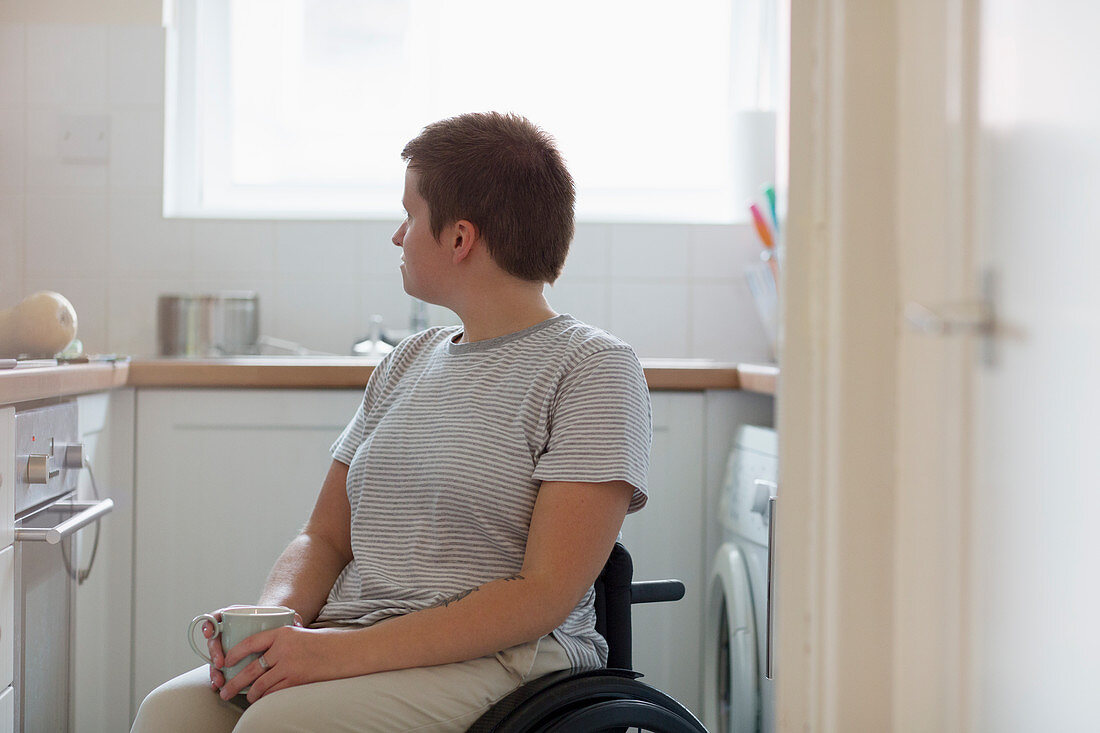 Thoughtful woman in wheelchair drinking tea