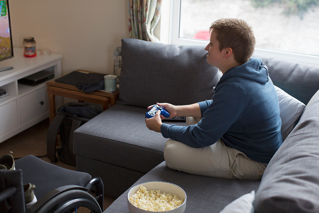 Young woman playing video game on sofa next to wheelchair