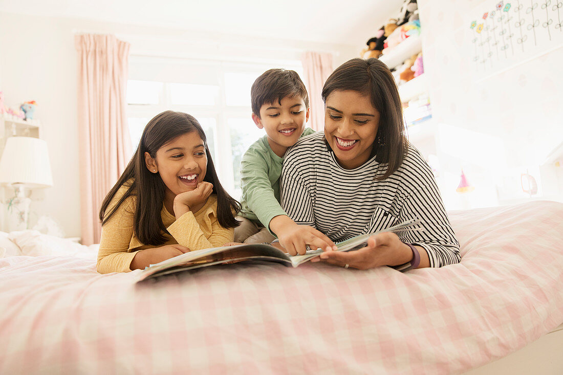Mother reading book to children on bed