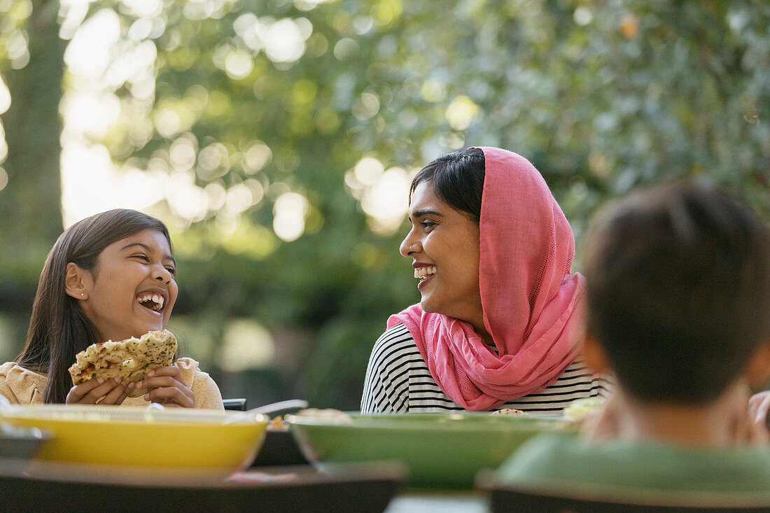 Mother in hijab and daughter laughing at dinner table