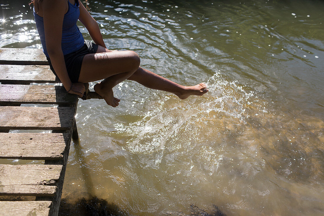 Girl on dock splashing foot in river water