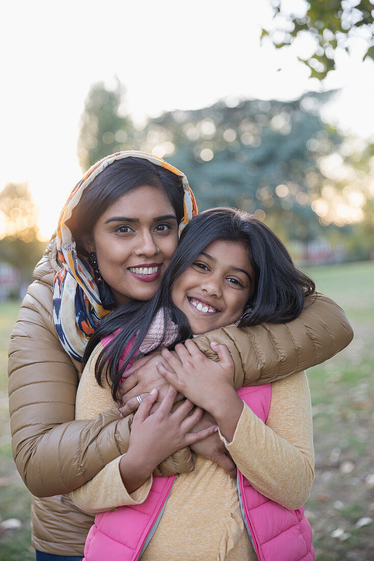 Portrait Muslim mother in hijab hugging daughter in park