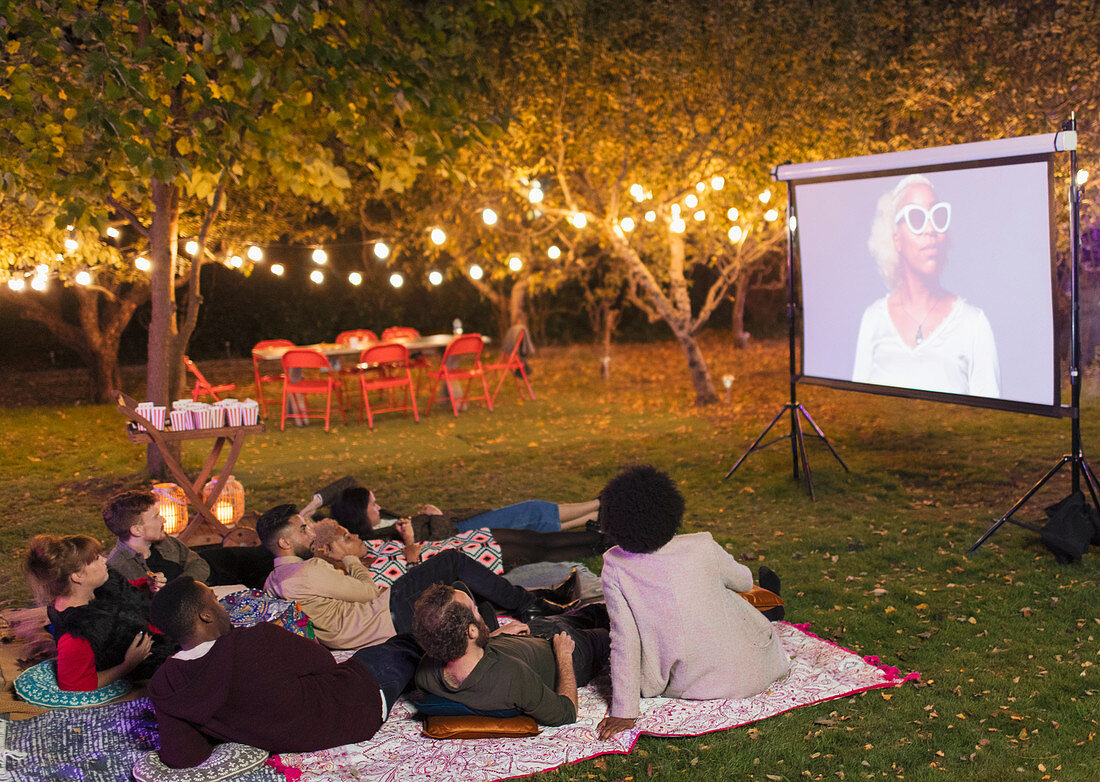 Friends watching movie on projection screen in backyard