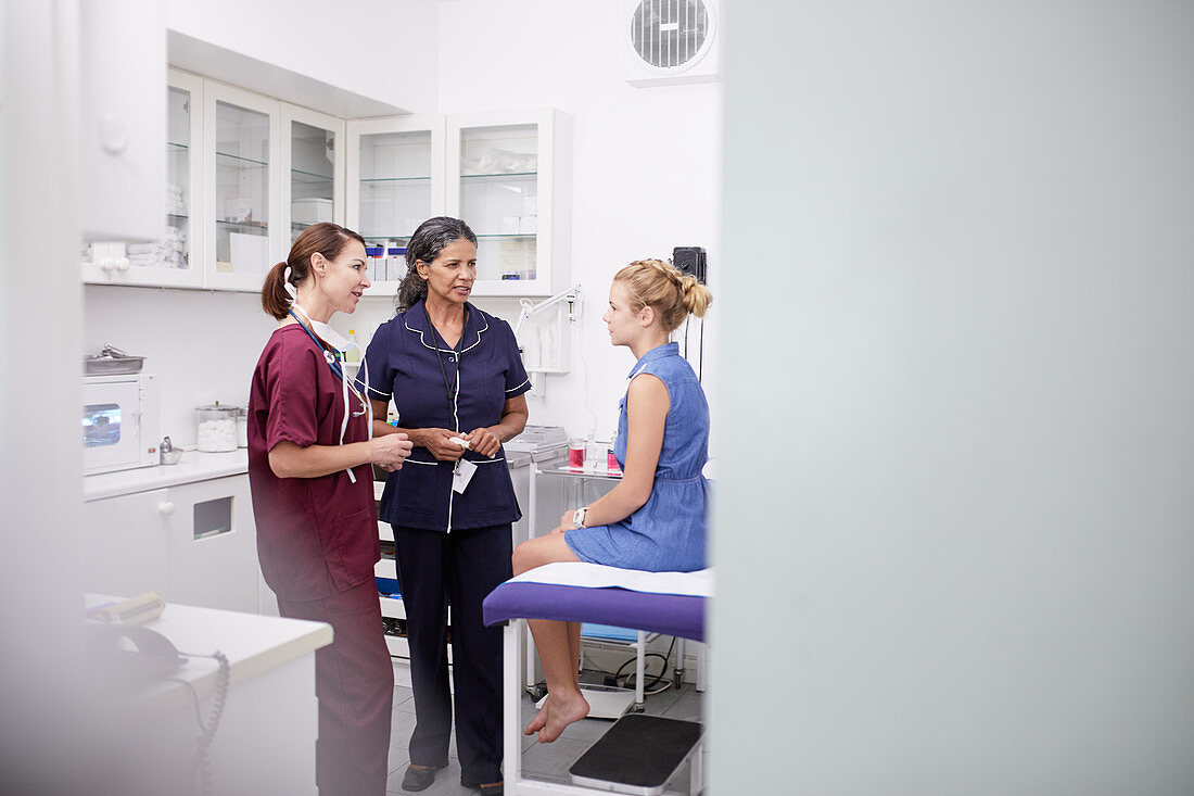 Female doctor and nurse talking to girl patient