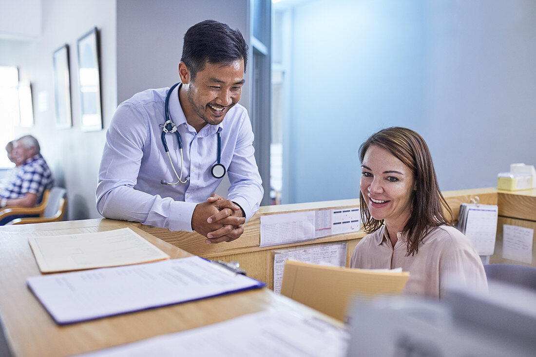 Smiling doctor and receptionist discussing medical record