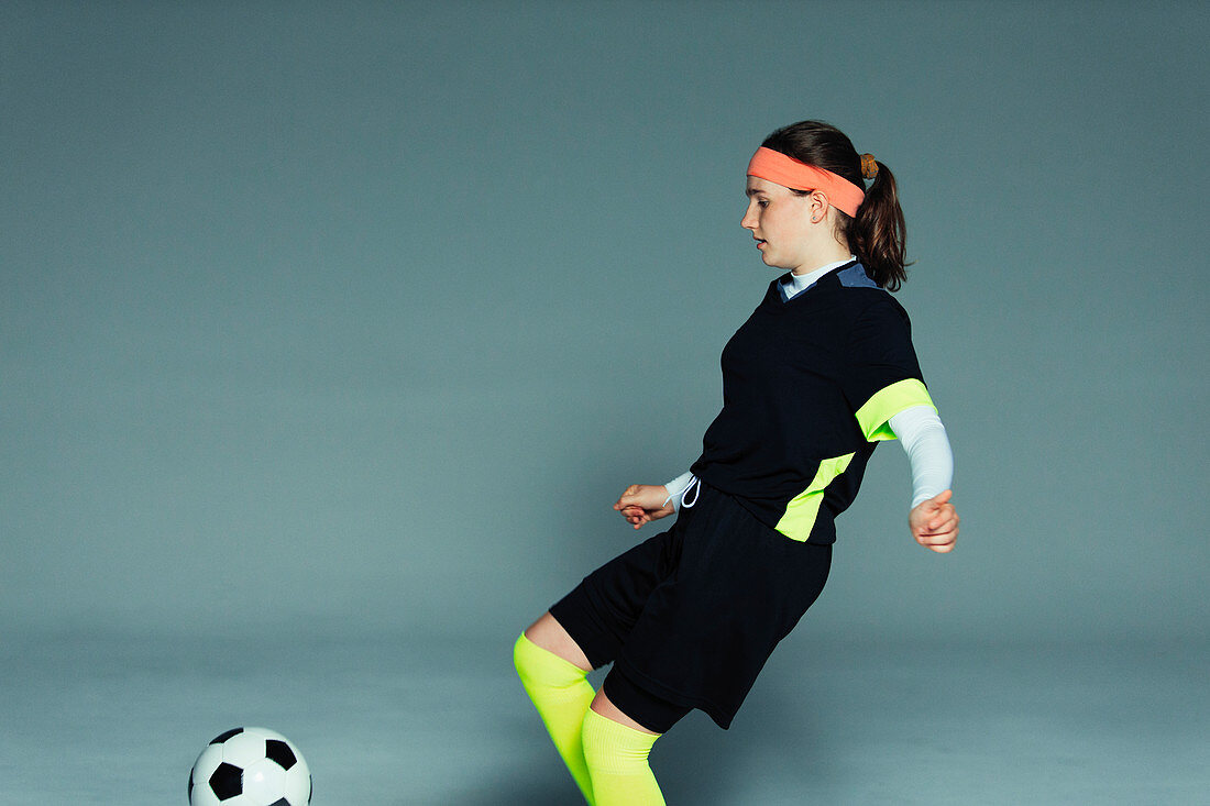 Teenage girl soccer player kicking soccer ball