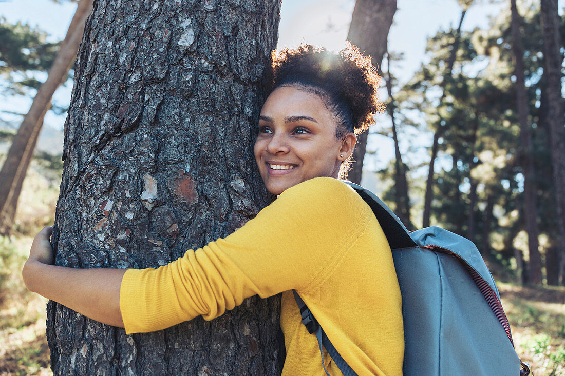 Happy, carefree young female hiker hugging tree