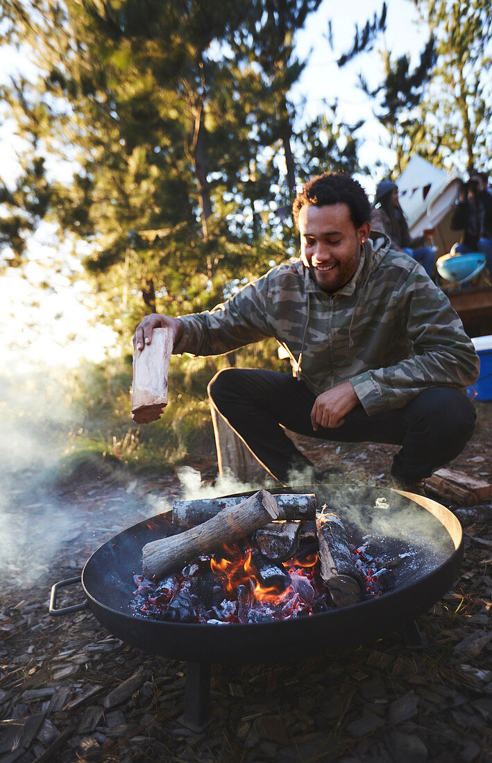 Man adding firewood to campsite campfire
