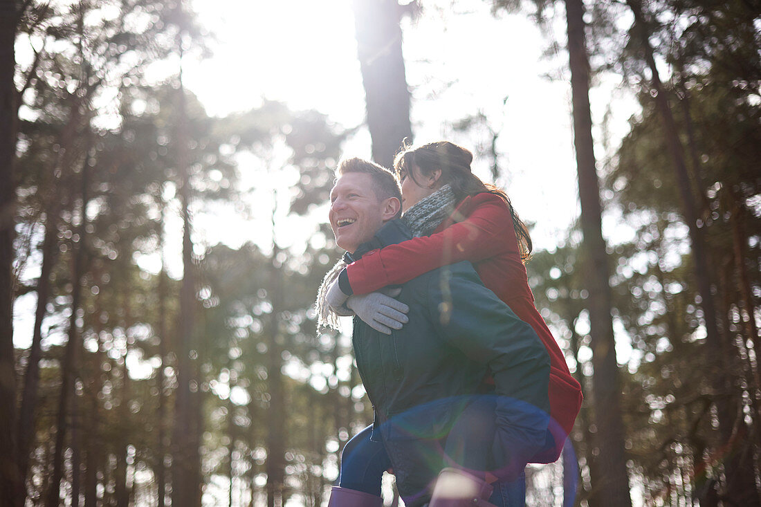 Happy, playful couple piggybacking in sunny woods
