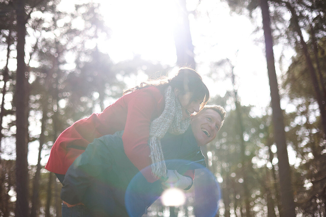 Couple piggybacking in sunny, autumn woods