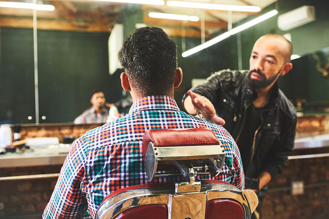 Male barber checking haircut of customer in barbershop
