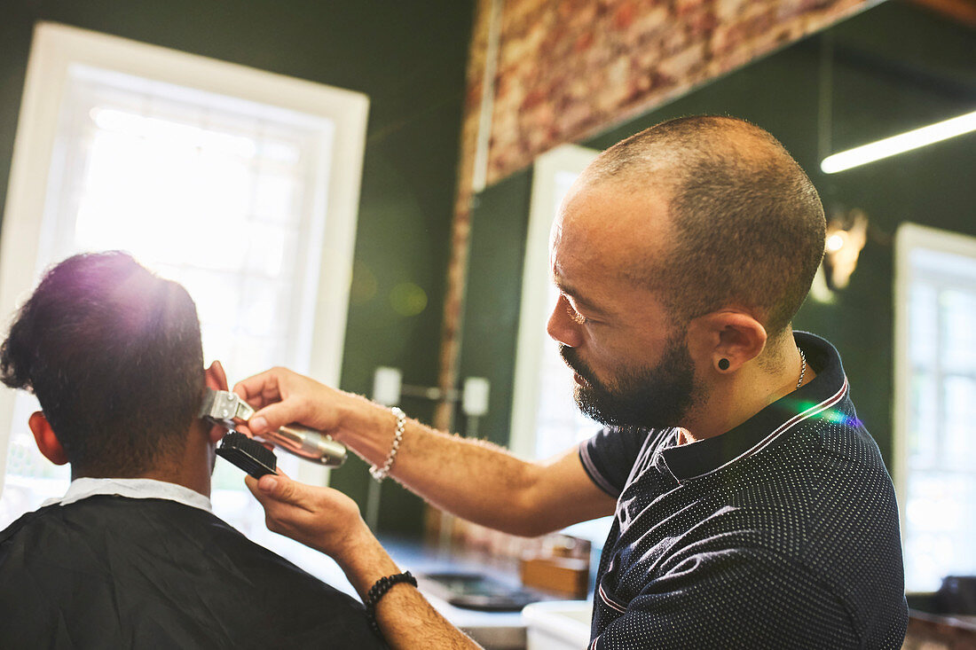 Male barber with trimmers giving customer haircut
