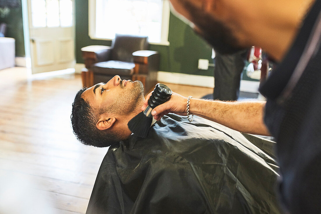 Male barber brushing face of customer in barbershop