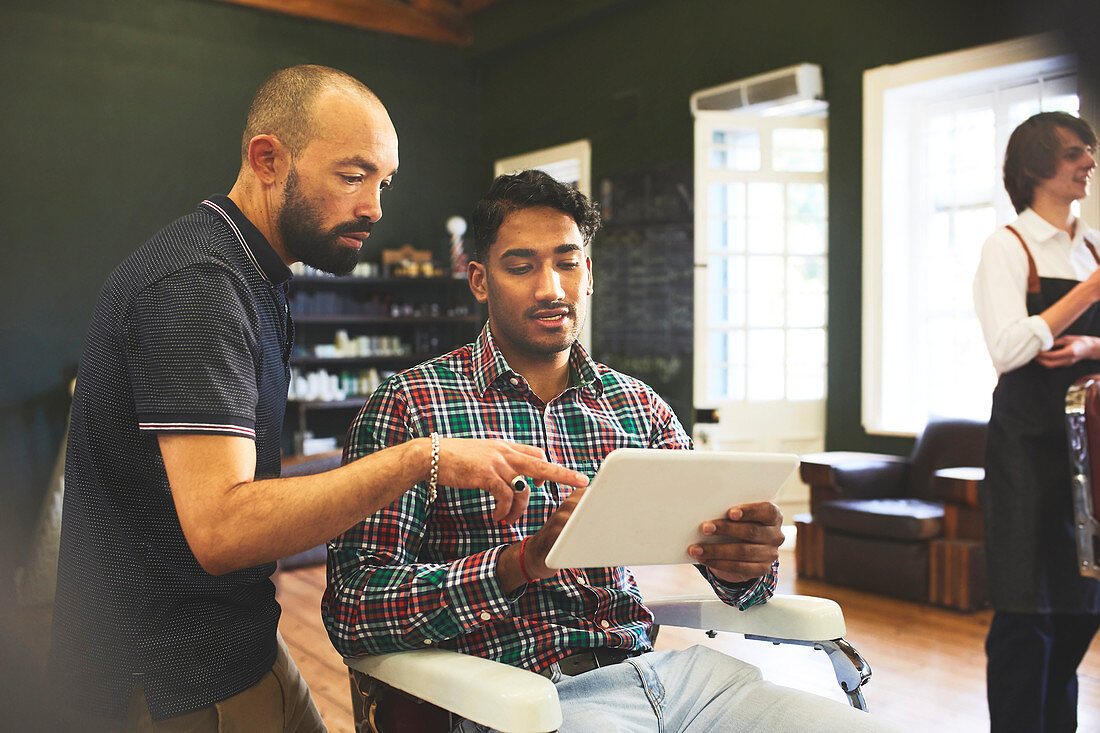 Male barber and customer with digital tablet talking