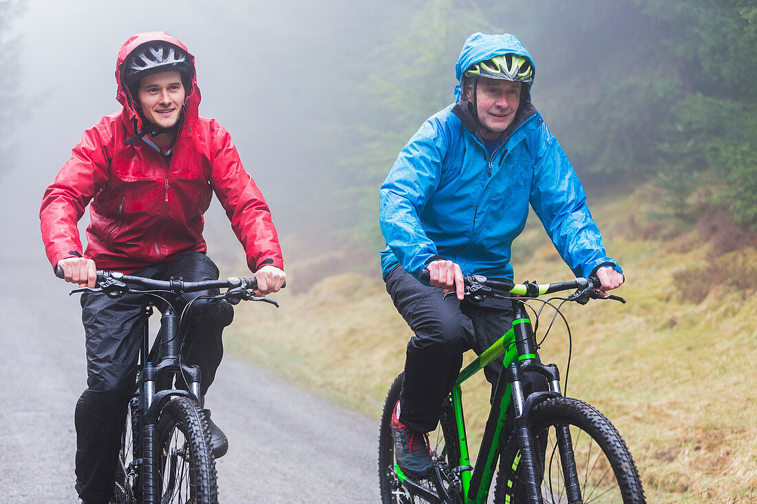 Father and son mountain biking in rain