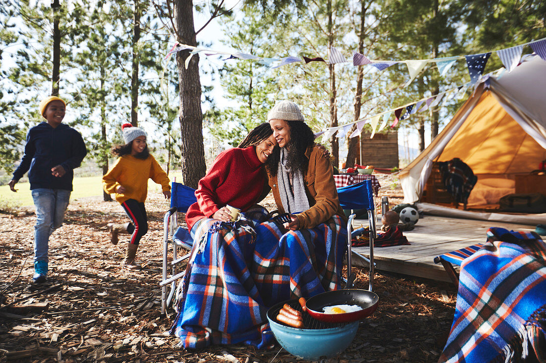 Lesbian couple with kids relaxing at campsite in woods