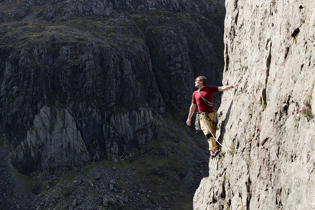 Male rock climber scaling tall rock face